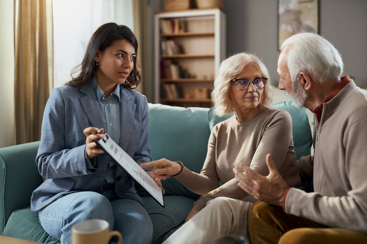Care advisor reviewing senior care placement options and documents with a senior couple during a family consultation in a warm living room