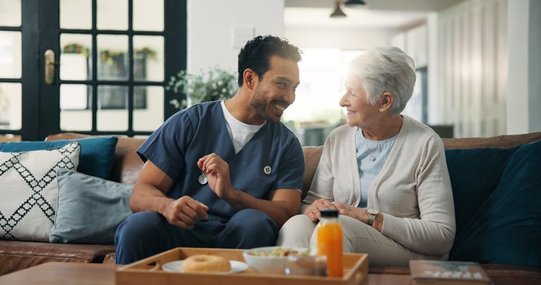 Hispanic nurse and man with elderly woman having breakfast on sofa at home