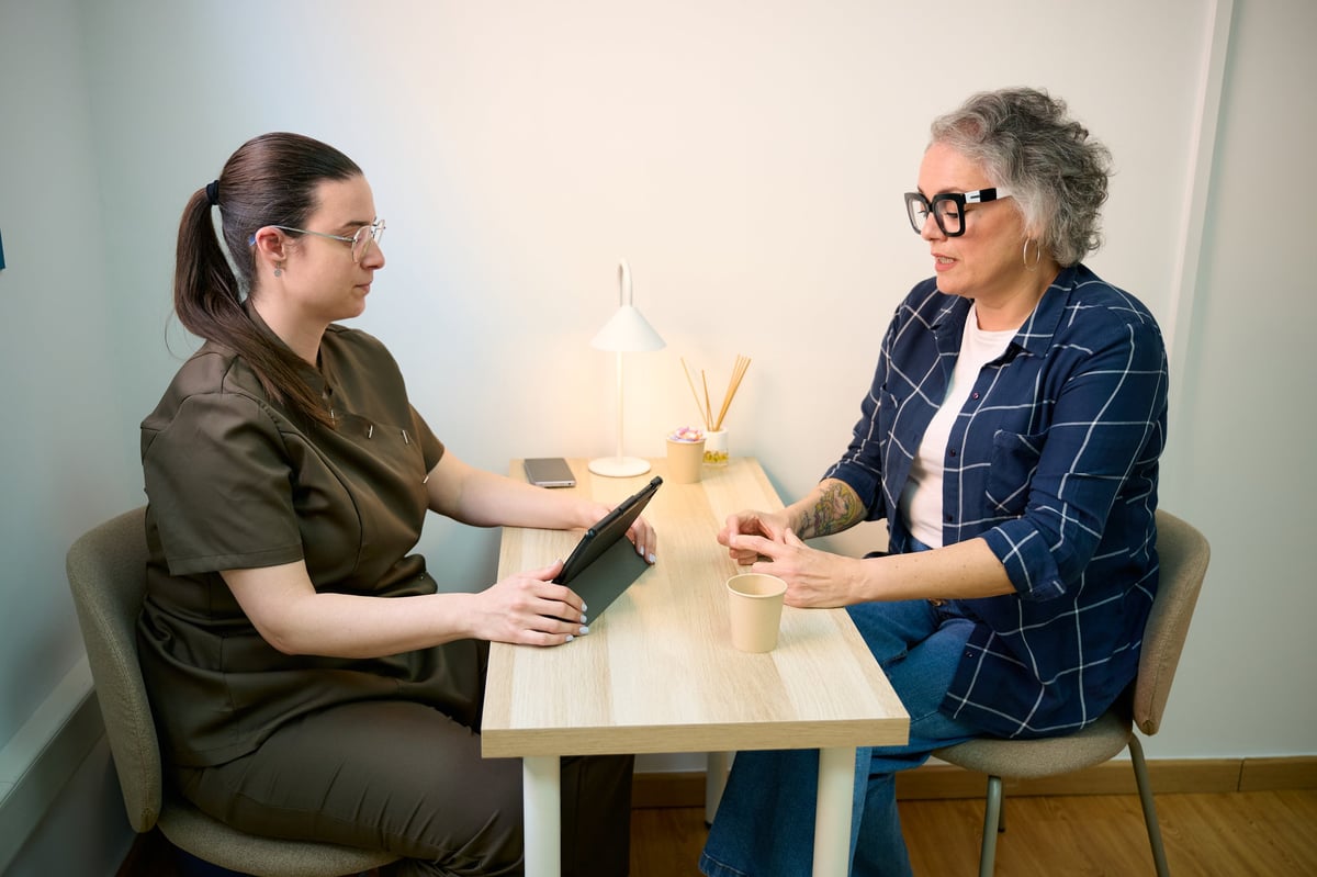 Healthcare professional holding a digital tablet, discussing with a mature adult patient in a modern office or clinic setting