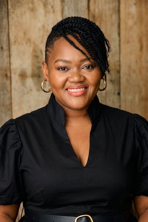 Professional headshot of a woman smiling at the camera wearing a black blouse against a wooden background